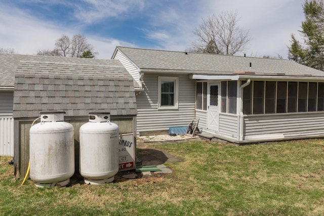 rear view of property featuring a lawn, a shingled roof, and a sunroom