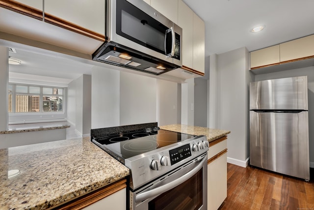 kitchen featuring stainless steel appliances, dark wood-type flooring, cream cabinets, light stone counters, and baseboards
