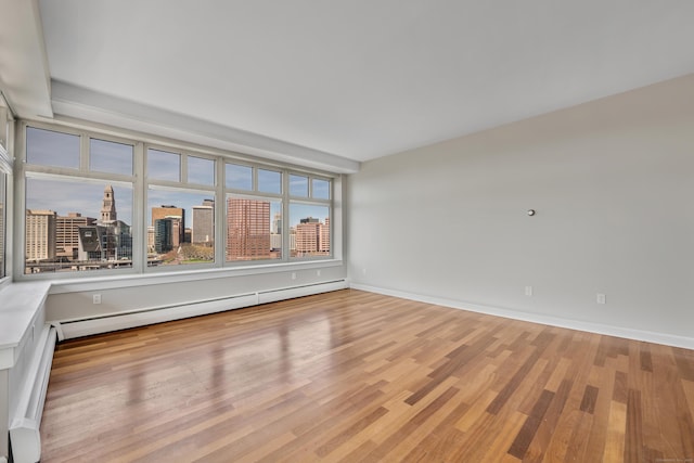 unfurnished room featuring light wood-type flooring, baseboards, a city view, and a baseboard radiator