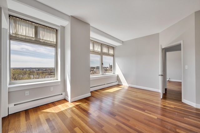 unfurnished room with a baseboard heating unit, wood finished floors, and baseboards