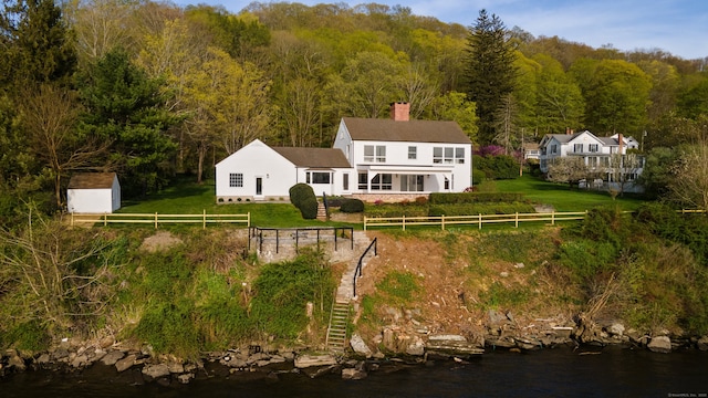 back of property with fence, stairs, a chimney, a forest view, and a lawn