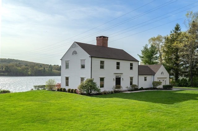 exterior space with a water view, roof with shingles, a front yard, and a chimney