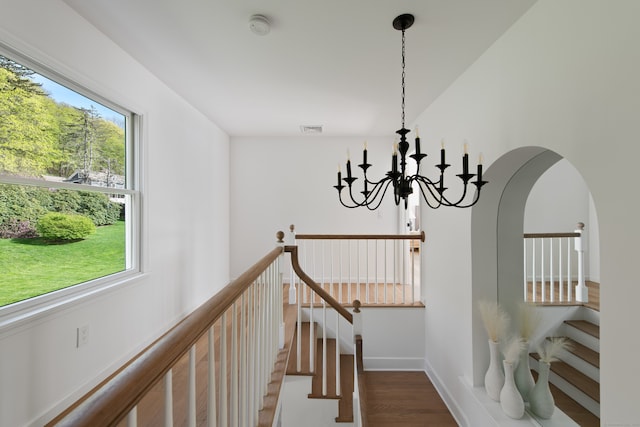 hallway featuring a healthy amount of sunlight, a notable chandelier, wood finished floors, and visible vents