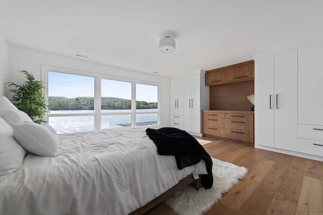 bedroom featuring a water view, multiple closets, visible vents, and light wood finished floors