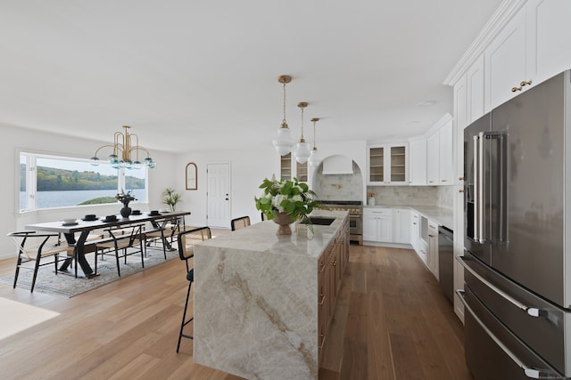 kitchen featuring an inviting chandelier, decorative backsplash, light stone countertops, a center island, and appliances with stainless steel finishes