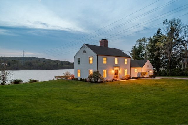 rear view of property with a lawn, a water view, and a chimney