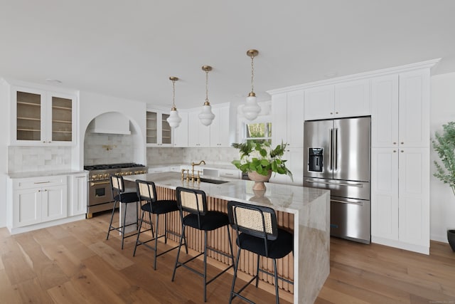 kitchen with high quality appliances, a sink, decorative backsplash, a center island with sink, and glass insert cabinets