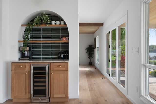 bar featuring light wood-style floors, backsplash, beverage cooler, and a wealth of natural light