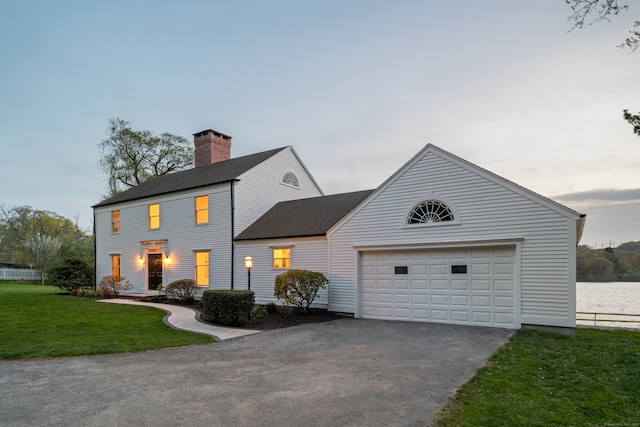 colonial house with a front lawn, aphalt driveway, roof with shingles, a chimney, and an attached garage