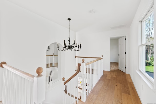 hallway featuring light wood-style floors, plenty of natural light, a chandelier, and an upstairs landing