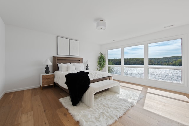 bedroom featuring a water view, baseboards, visible vents, and wood finished floors