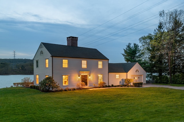colonial inspired home featuring a chimney, an attached garage, driveway, and a front yard