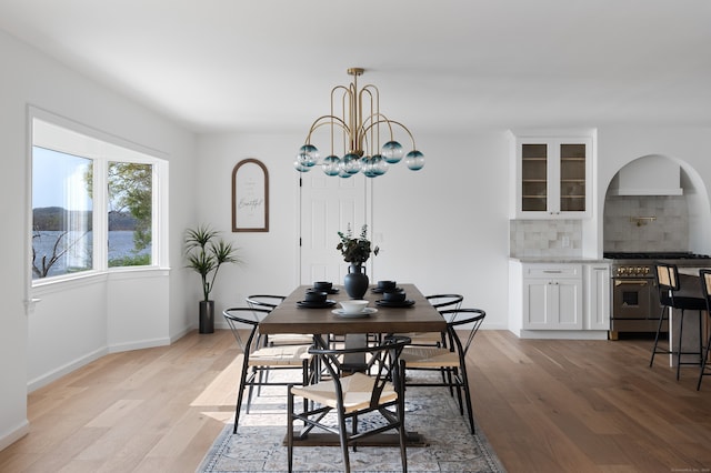 dining space with light wood-style floors, arched walkways, baseboards, and an inviting chandelier