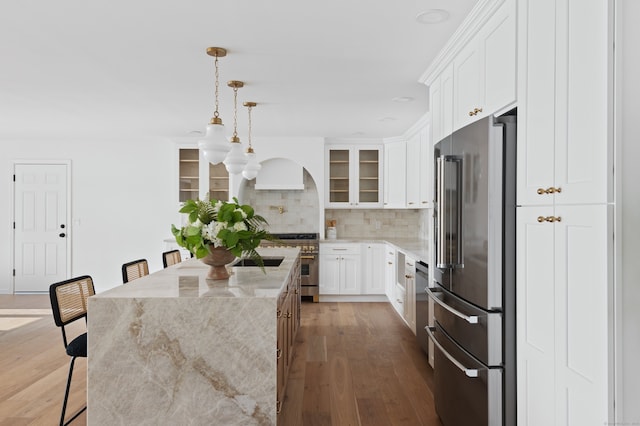 kitchen with light stone counters, a center island, decorative backsplash, premium appliances, and glass insert cabinets