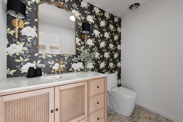 half bath with toilet, wallpapered walls, baseboards, and vanity