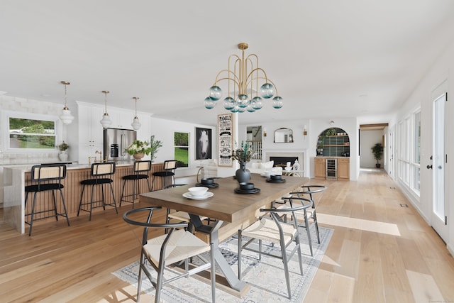 dining room featuring light wood-style floors, wine cooler, a healthy amount of sunlight, and an inviting chandelier