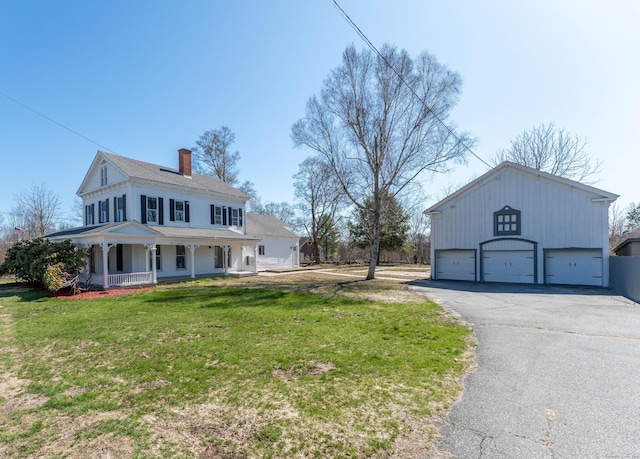 view of front of home with a front lawn, covered porch, a chimney, and a detached garage