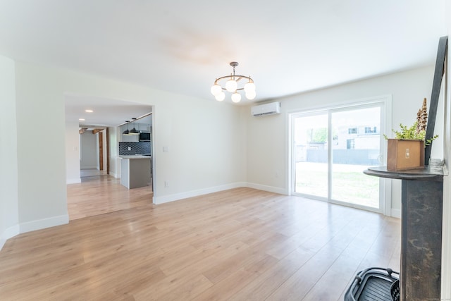 unfurnished living room featuring an inviting chandelier, baseboards, a wall mounted AC, and light wood-type flooring
