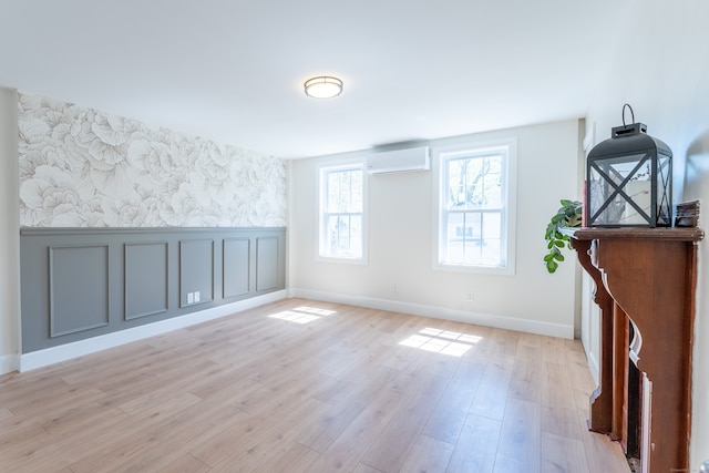 interior space featuring wainscoting, baseboards, wallpapered walls, a wall unit AC, and light wood-style flooring