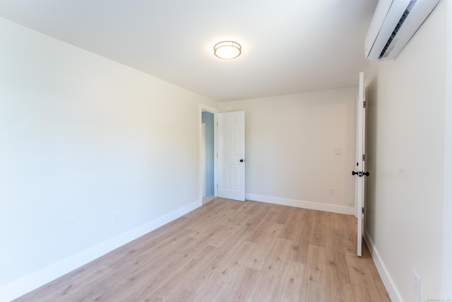 spare room with light wood-style floors, a wall mounted air conditioner, and baseboards
