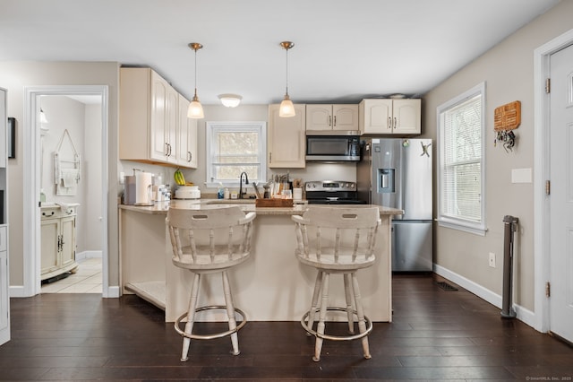 kitchen featuring dark wood finished floors, a peninsula, stainless steel appliances, and pendant lighting