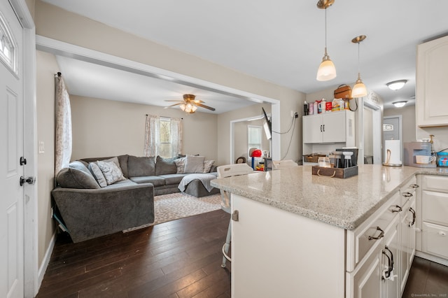 kitchen with white cabinets, dark wood-style floors, a ceiling fan, light stone countertops, and a peninsula