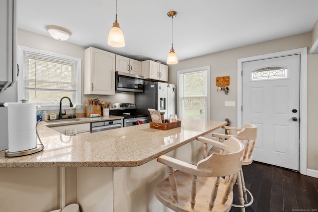 kitchen featuring a peninsula, a kitchen breakfast bar, a sink, light stone counters, and appliances with stainless steel finishes