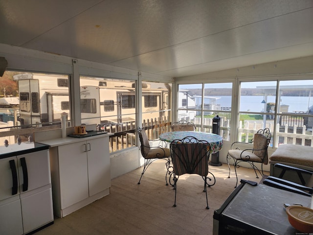 sunroom / solarium featuring wood finished floors, a sink, a water view, and lofted ceiling