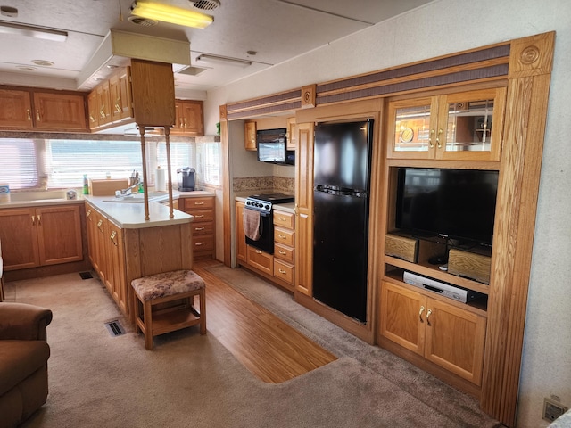 kitchen featuring light colored carpet, brown cabinets, a sink, light countertops, and black appliances