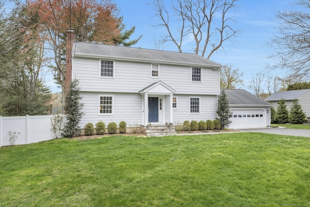 colonial home featuring an attached garage, fence, a chimney, a front lawn, and driveway