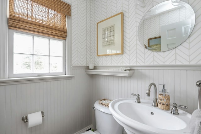 half bath featuring a sink, toilet, a wainscoted wall, and wallpapered walls