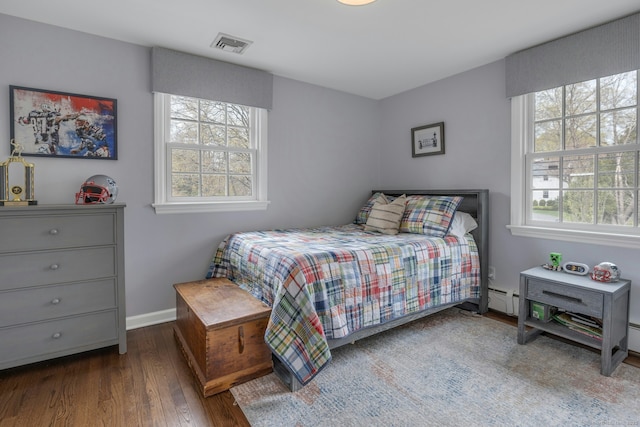 bedroom with visible vents, wood finished floors, baseboards, and a baseboard heating unit