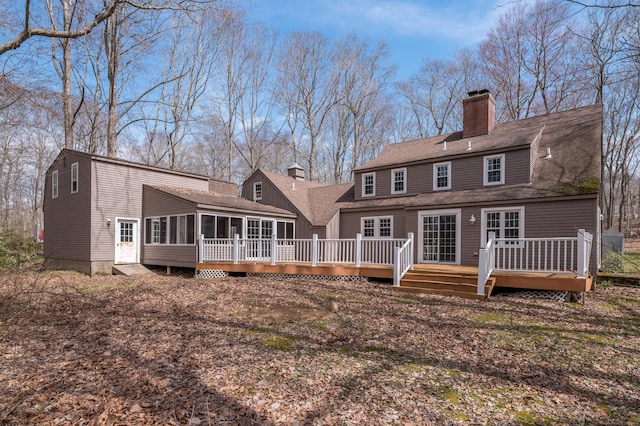 rear view of property featuring a chimney, a sunroom, a deck, and a shingled roof