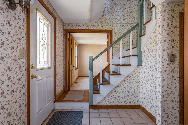 foyer featuring light tile patterned floors, wallpapered walls, baseboards, and stairway