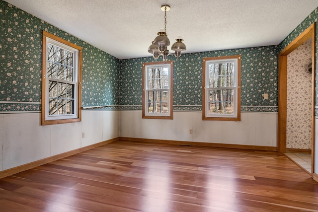 unfurnished dining area featuring wallpapered walls, wood finished floors, an inviting chandelier, and a textured ceiling