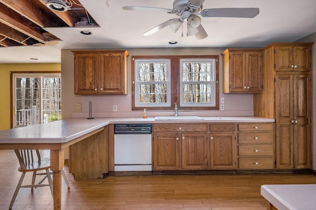 kitchen with a sink, brown cabinets, dishwasher, light countertops, and a peninsula