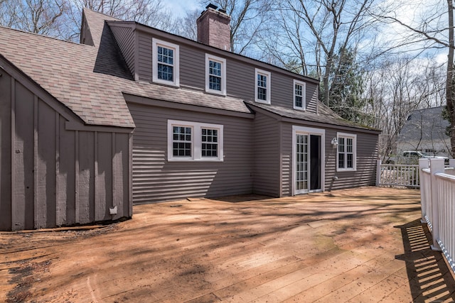rear view of house with board and batten siding, a wooden deck, a chimney, and roof with shingles