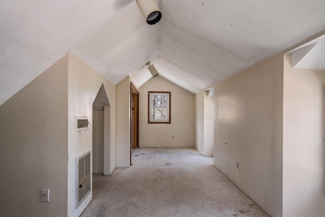 additional living space with a textured ceiling, vaulted ceiling, visible vents, and light carpet