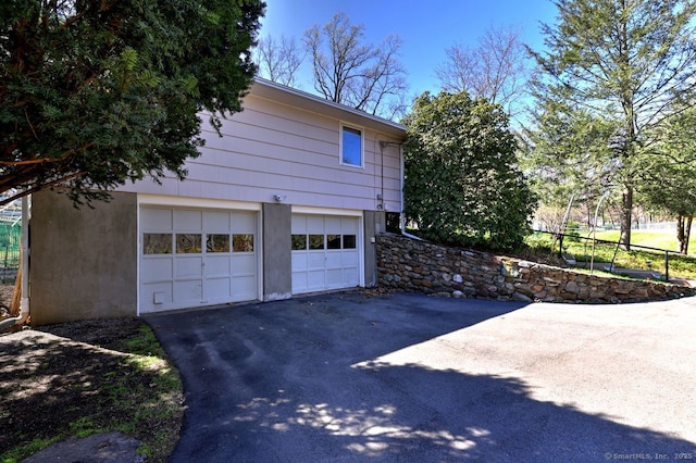 view of side of property with a garage, asphalt driveway, and stucco siding