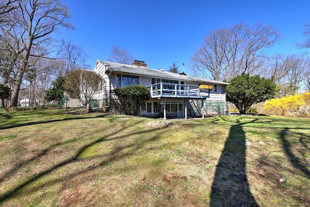 rear view of house featuring a chimney, a wooden deck, and a lawn