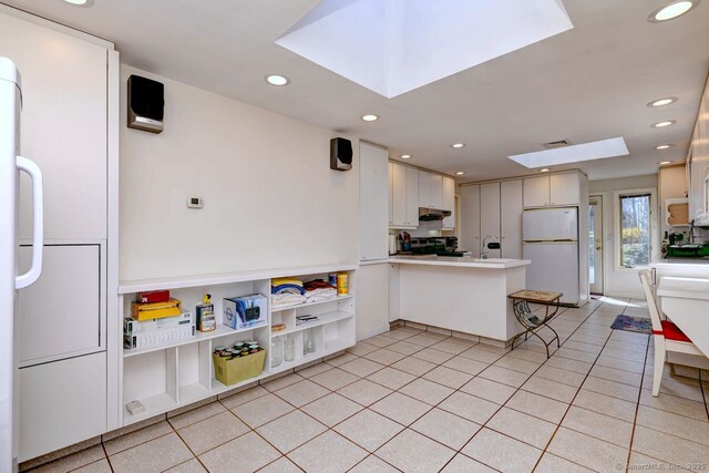 kitchen with a skylight, freestanding refrigerator, a peninsula, range, and recessed lighting