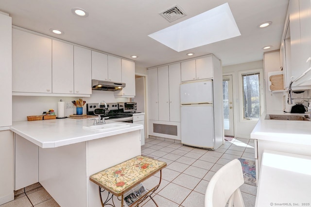 kitchen with freestanding refrigerator, under cabinet range hood, a skylight, a peninsula, and recessed lighting