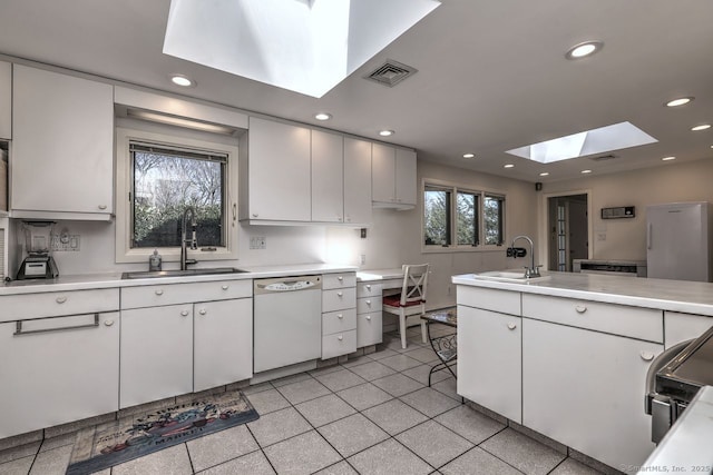 kitchen with a skylight, white appliances, a sink, recessed lighting, and light countertops