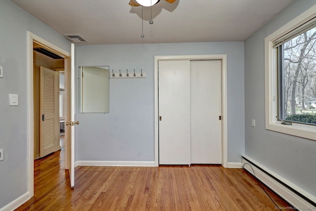 unfurnished bedroom with a baseboard radiator, light wood-style floors, multiple windows, and baseboards
