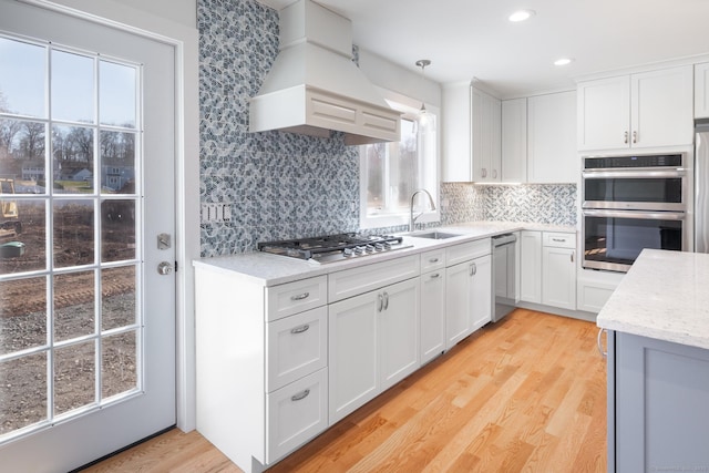 kitchen featuring white cabinets, stainless steel appliances, a sink, tasteful backsplash, and custom range hood