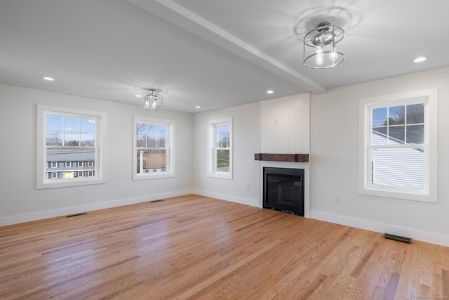 unfurnished living room with a wealth of natural light, light wood finished floors, a glass covered fireplace, and visible vents