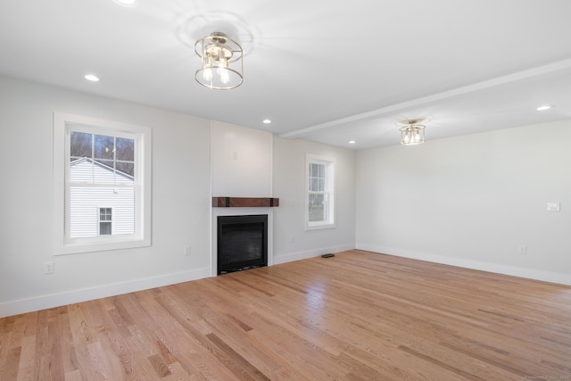 unfurnished living room with light wood finished floors, baseboards, a glass covered fireplace, and a healthy amount of sunlight