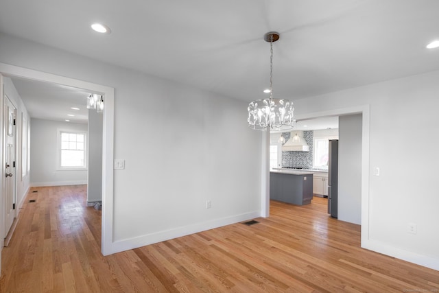 unfurnished dining area featuring baseboards, an inviting chandelier, visible vents, and light wood-type flooring
