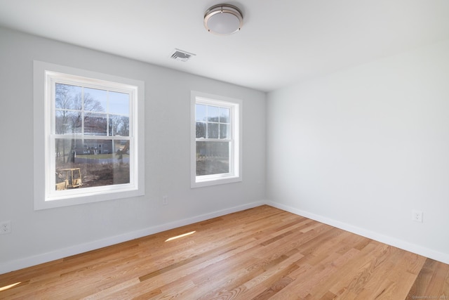 spare room with wood finished floors, visible vents, and baseboards