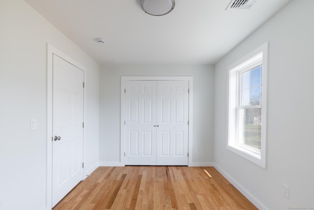 unfurnished bedroom featuring baseboards, light wood finished floors, visible vents, and a closet